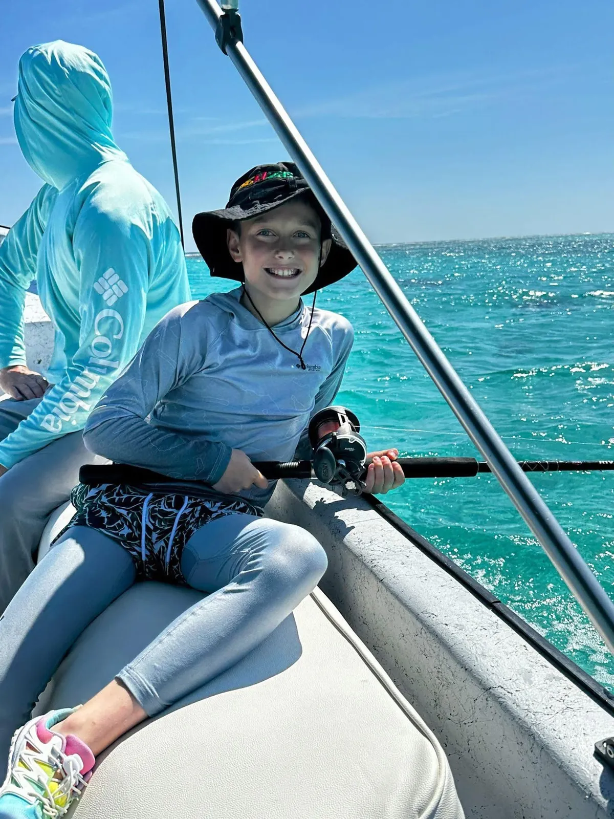 Young angler smiling with a rod on turquoise water